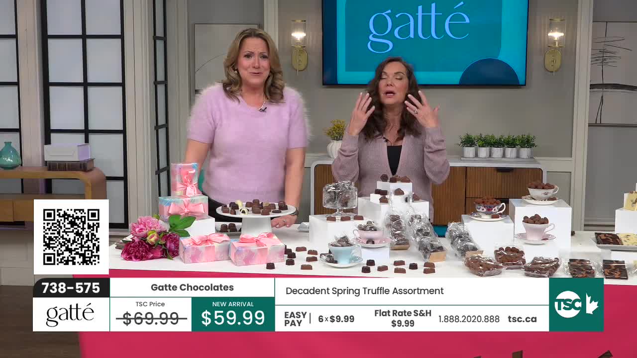 Two women stand behind a table laden with Gatte chocolates. The chocolates are arranged on tiered stands and in small decorative cups.