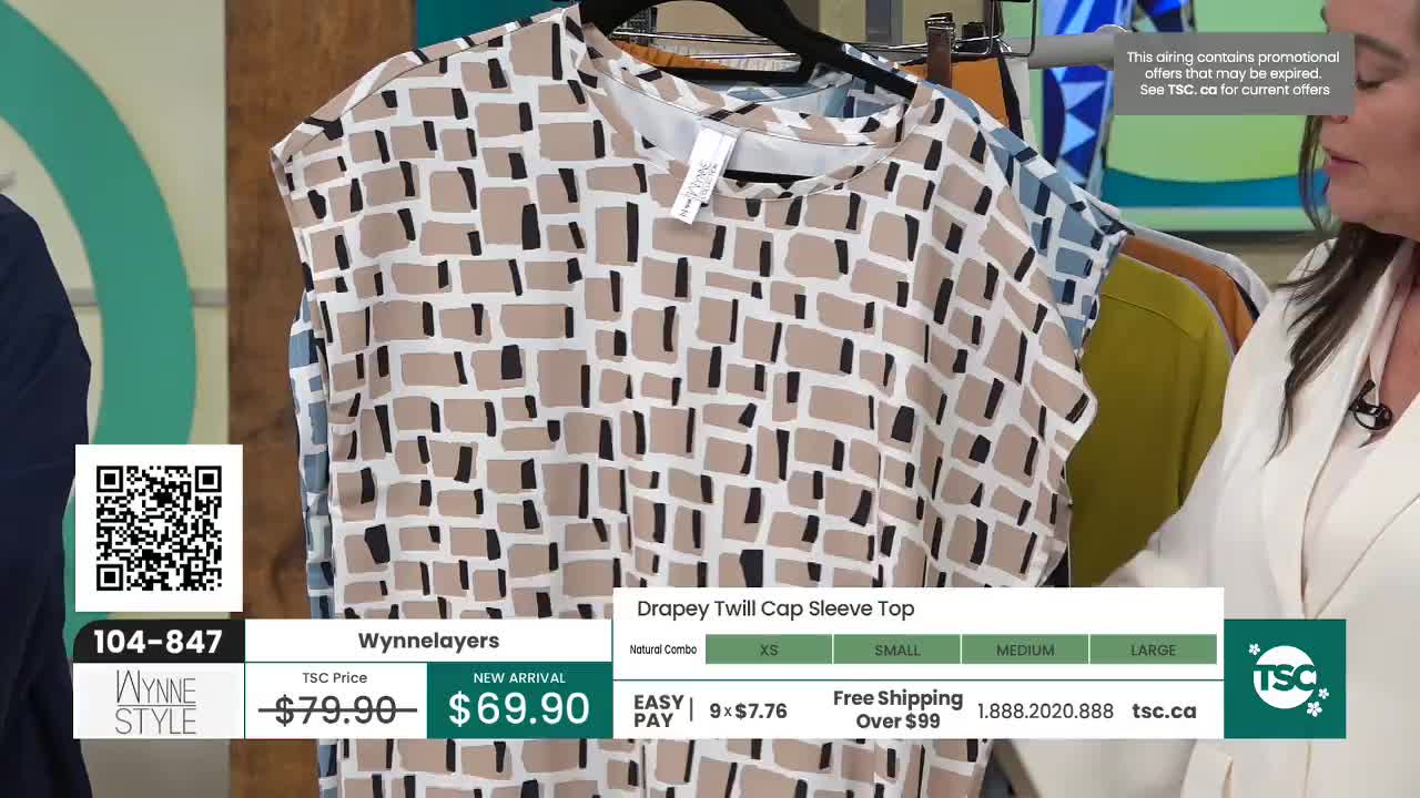 A woman in a cream jacket gestures towards a beige and black patterned top hanging on a rack. The top is a "Drapey Twill Cap Sleeve Top" from WynneLayers, currently priced at $69.90.