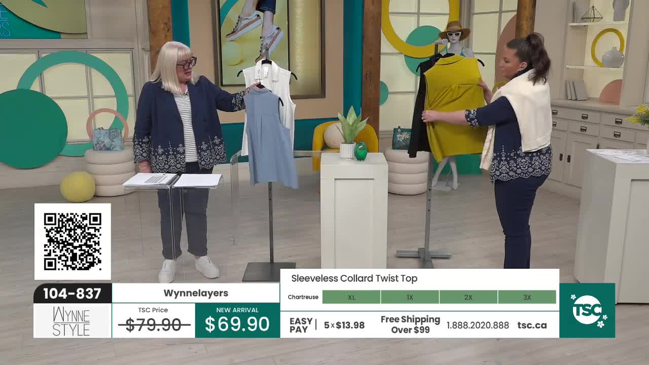 A woman in a blue jacket holds up a light blue sleeveless top. Another woman adjusts a bright yellow top on a mannequin.