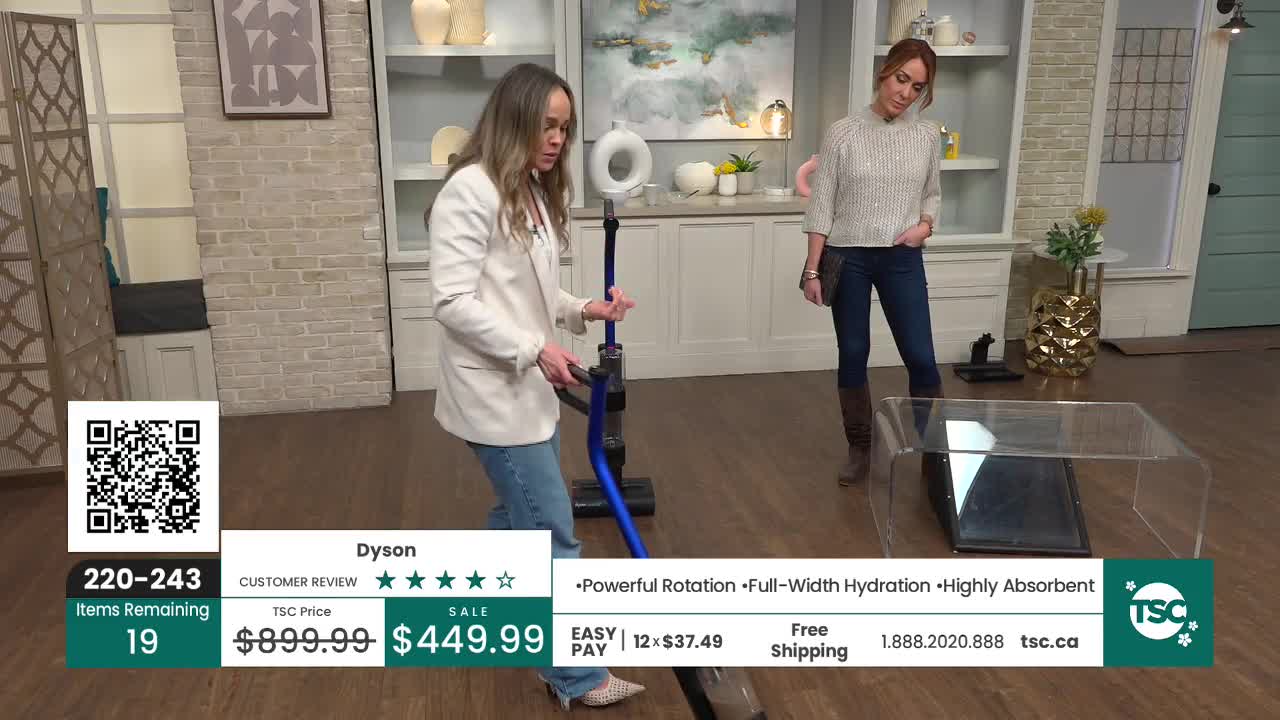A woman in a white blazer demonstrates a blue vacuum cleaner on the TSC set. Another woman stands nearby, watching the demonstration. A woman in a white blazer demonstrates a blue vacuum cleaner on the TSC set. Another woman stands nearby, watching the demonstration.