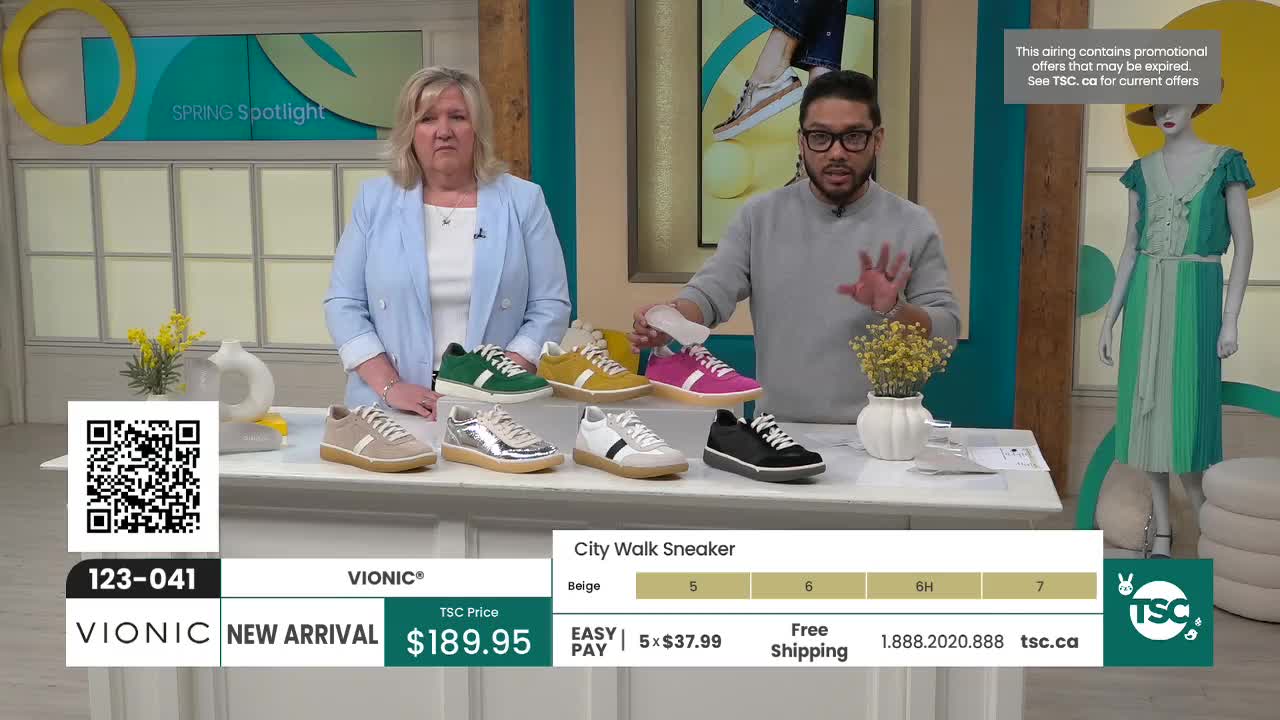 A woman in a light blue blazer and a man in a grey sweater stand behind a display of colorful Vionic "City Walk Sneakers." The shoes are arranged in two rows on a white table, showcasing options in beige, silver, white, green, yellow, and fuchsia. A woman in a light blue blazer and a man in a grey sweater stand behind a display of colorful Vionic "City Walk Sneakers." The shoes are arranged in two rows on a white table, showcasing options in beige, silver, white, green, yellow, and fuchsia.