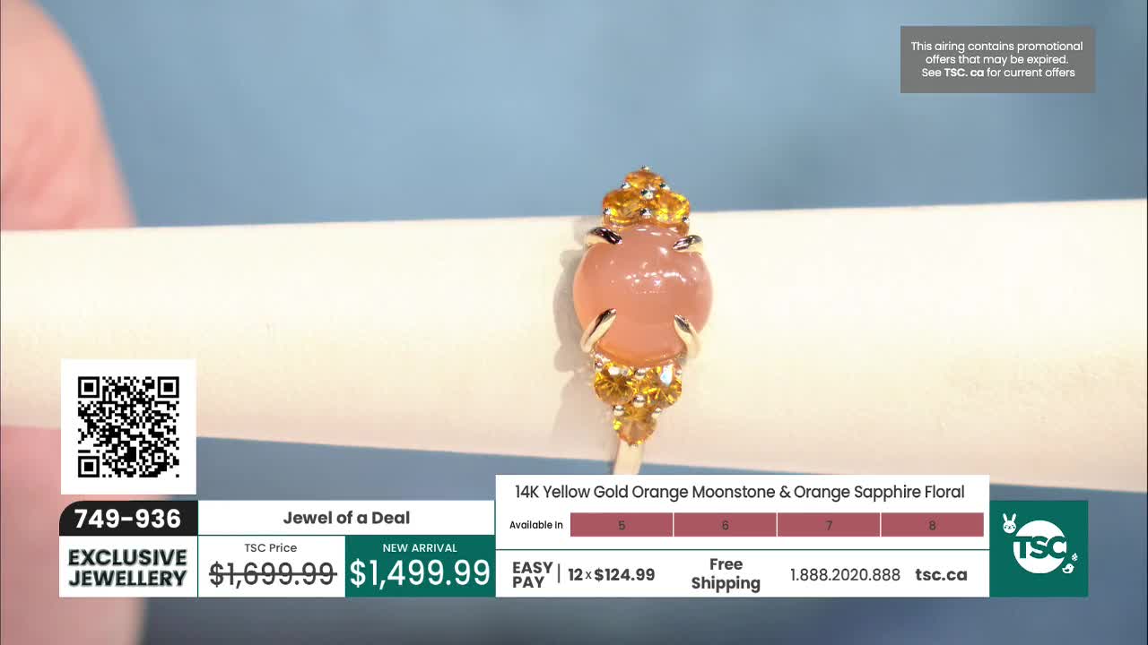 A peach-colored moonstone ring with small orange sapphires sits on a white stand. The ring is a new arrival, priced at $1,499.99.