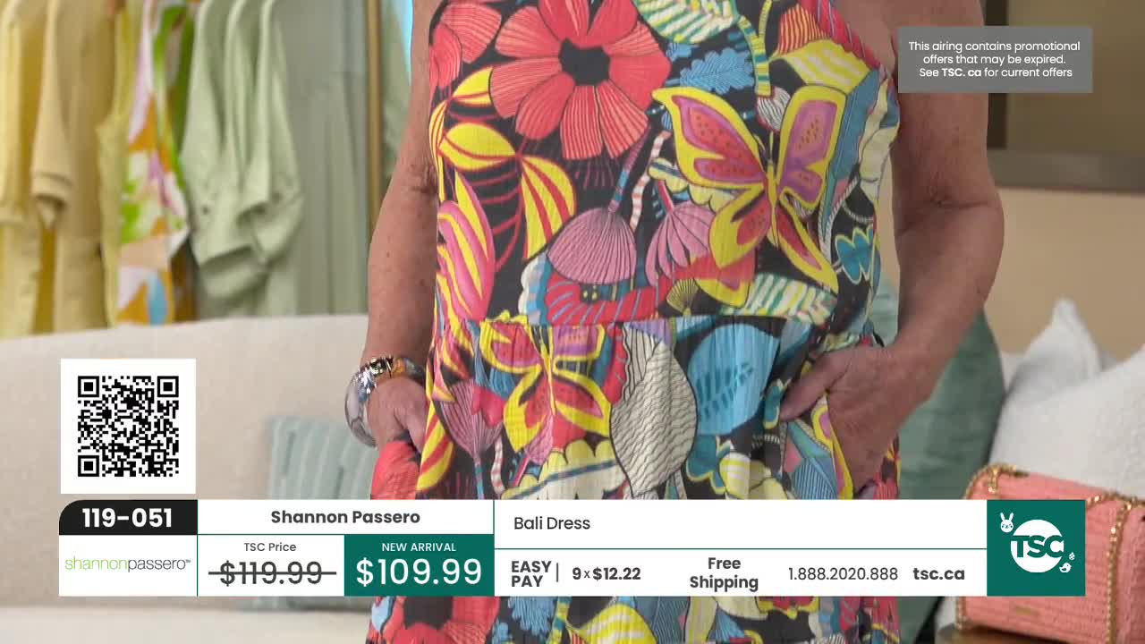 A woman models a vibrant, floral print dress. The fabric is a riot of pink, yellow, and blue flowers and butterflies.