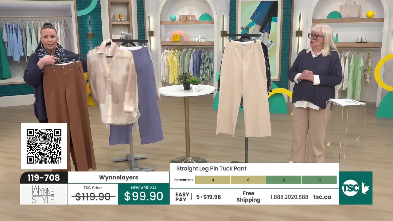 A woman on the left holds up a pair of brown trousers, while another woman on the right stands with her hands clasped. Behind them, clothes hang on racks and mannequins display more garments. A woman on the left holds up a pair of brown trousers, while another woman on the right stands with her hands clasped. Behind them, clothes hang on racks and mannequins display more garments.