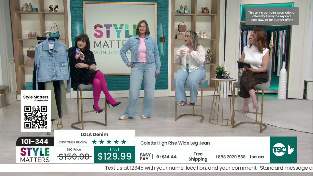 A woman stands in light-wash denim jeans and a matching jacket, her hands on her hips. Another woman, seated, gestures with her hands while discussing the outfit. A woman stands in light-wash denim jeans and a matching jacket, her hands on her hips. Another woman, seated, gestures with her hands while discussing the outfit.