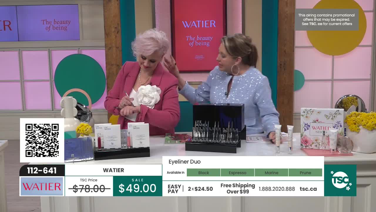 One woman applies a product to her wrist while another gestures towards a display of makeup. The TSC logo and product information are visible on screen. One woman applies a product to her wrist while another gestures towards a display of makeup. The TSC logo and product information are visible on screen.