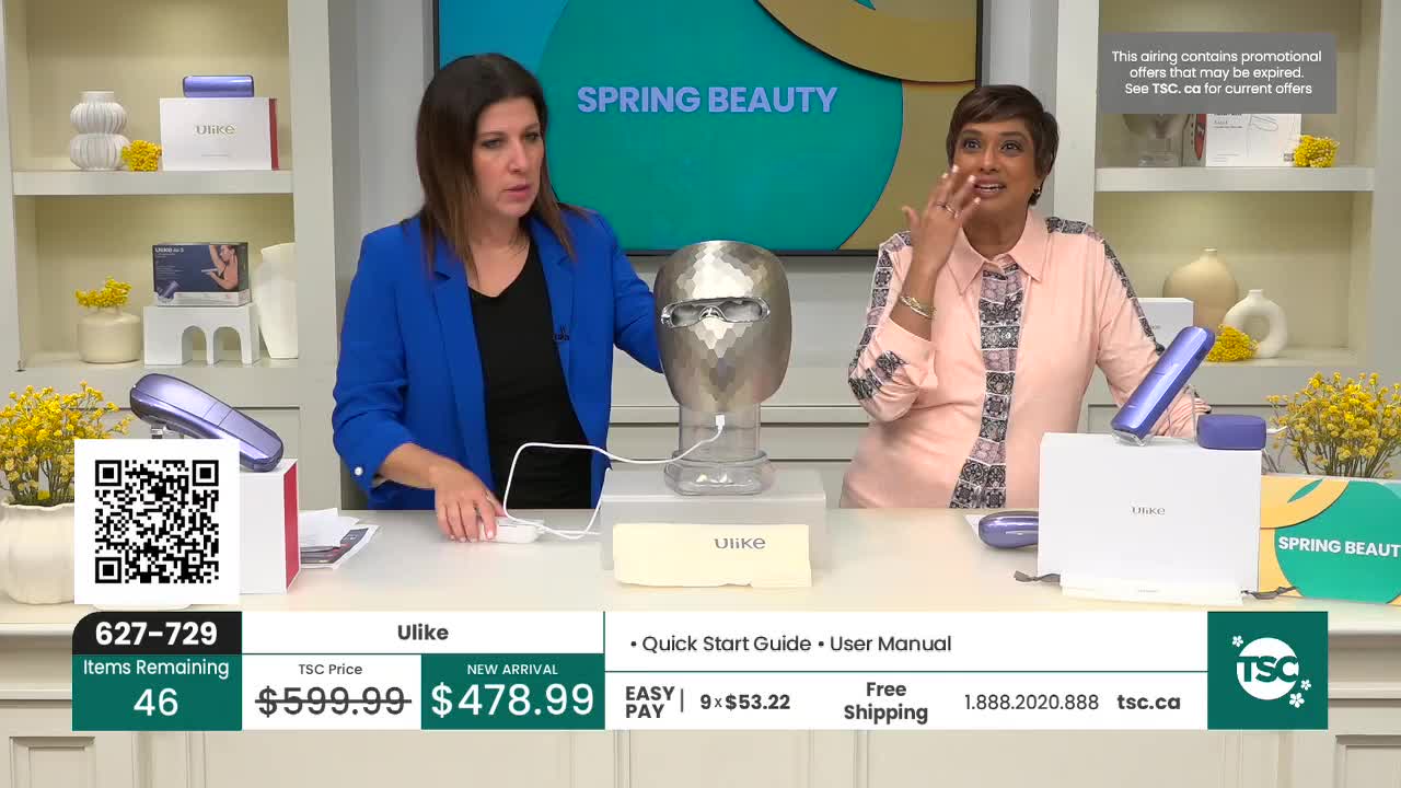 A woman in a blue jacket gestures towards a silver, faceted head-shaped device. Another woman, wearing a patterned pink top, touches her face as she speaks. A woman in a blue jacket gestures towards a silver, faceted head-shaped device. Another woman, wearing a patterned pink top, touches her face as she speaks.