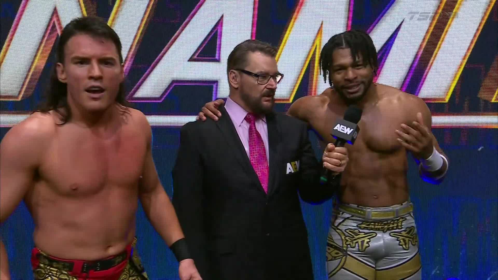 The wrestler on the right gestures with his hands while speaking into a microphone, flanked by a suited man and another wrestler. TSN2 is broadcasting a wrestling event, and the crowd is waiting to hear what's next.

