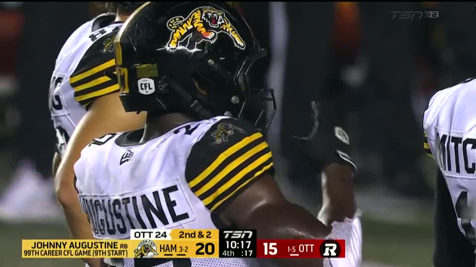 The Hamilton Tiger-Cats player, Augustine, stands on the sidelines, his black helmet with the tiger logo facing the field. The TSN2 broadcast shows the score and the game clock.
