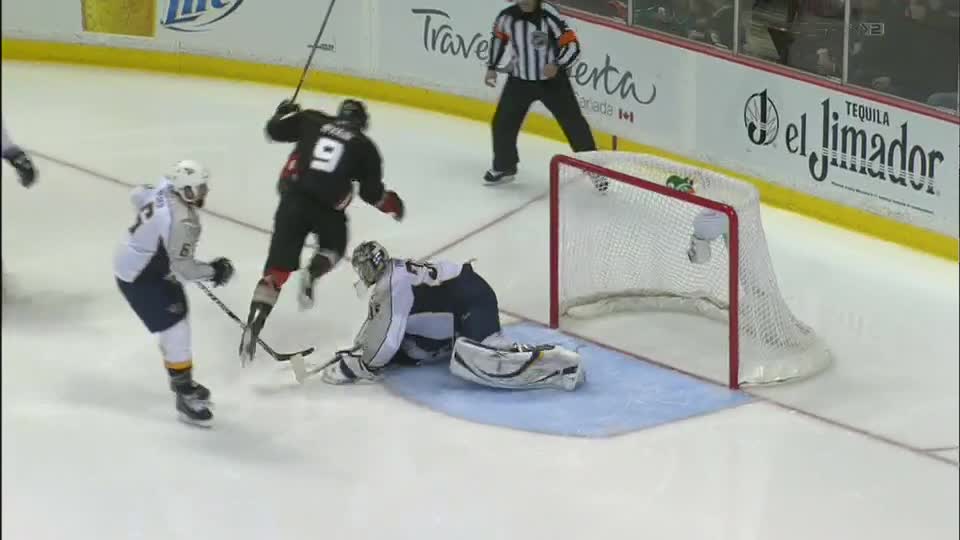 The goalie is down, sprawled out in front of the net. A player in black, number 9, is skating towards the goal, stick raised.
