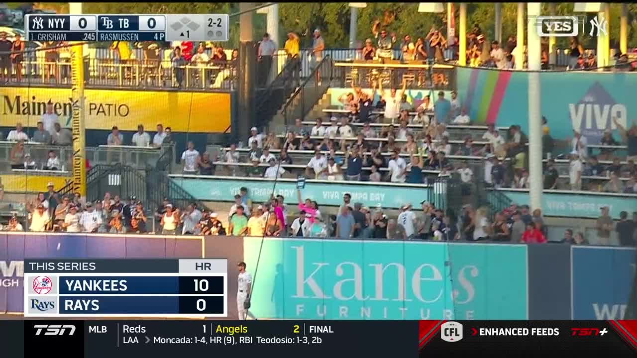 The scoreboard shows the Yankees are crushing the Rays, with a score of 10-0.  Fans in the stands are on their feet, many with their arms raised in celebration.
