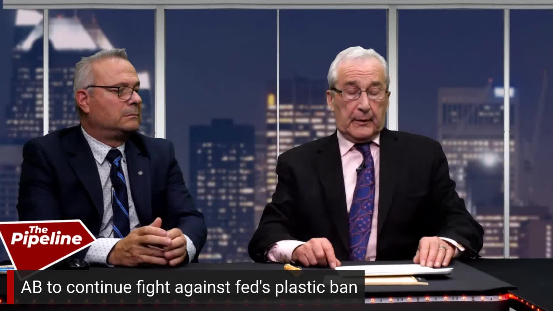 Two men in suits sit behind a desk; one is speaking, gesturing with his hands while the other looks on. The chyron at the bottom of the screen reads "AB to continue fight against fed's plastic ban."
