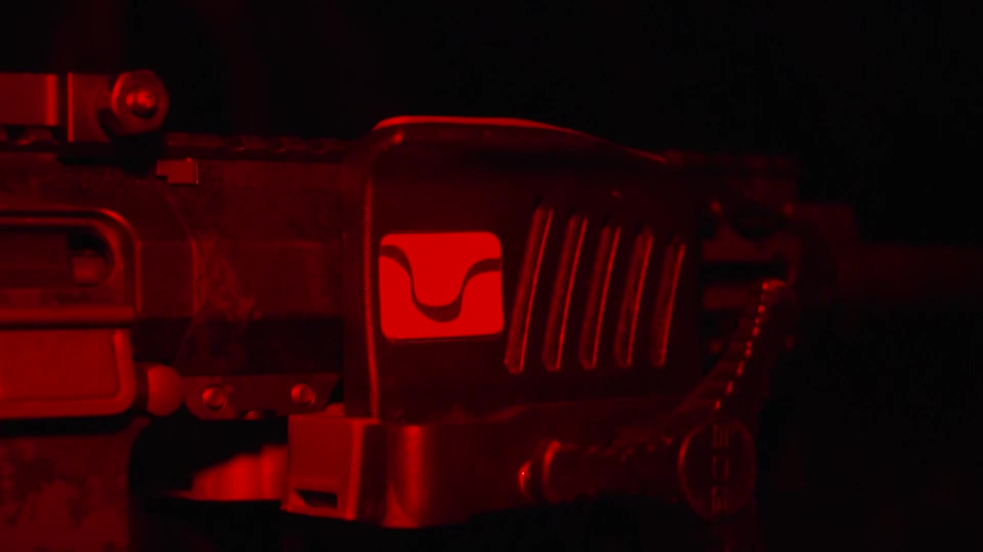 The Wild TV logo glows red on the side of a rifle, its shape clearly defined in the darkness. Vertical lines and a few screws are visible, suggesting the weapon's construction.
