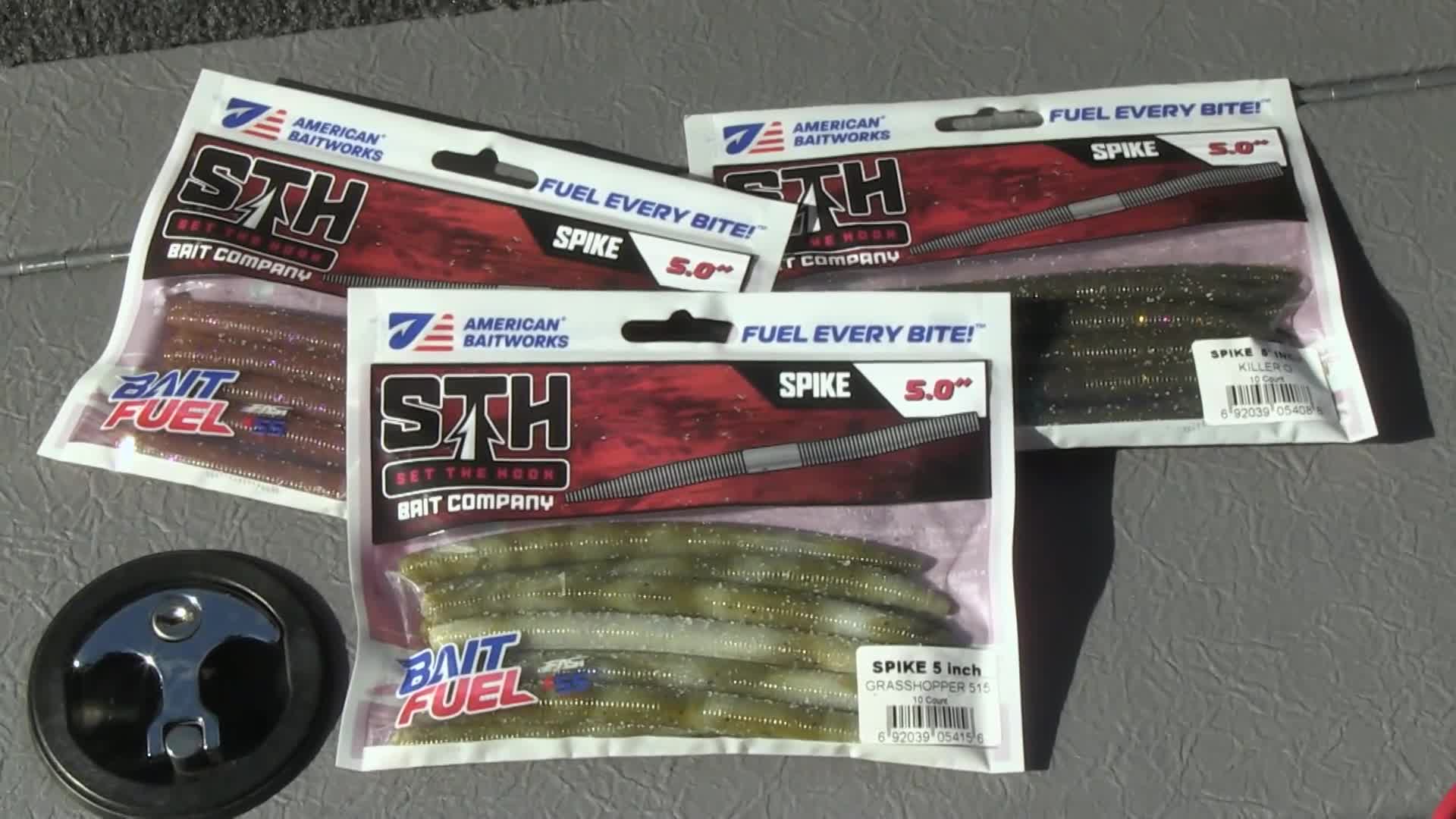 Three packs of American Baitworks STH Spike worms lie on a textured surface. A chrome boat latch sits to the left of the bait packages. Three packs of American Baitworks STH Spike worms lie on a textured surface. A chrome boat latch sits to the left of the bait packages.