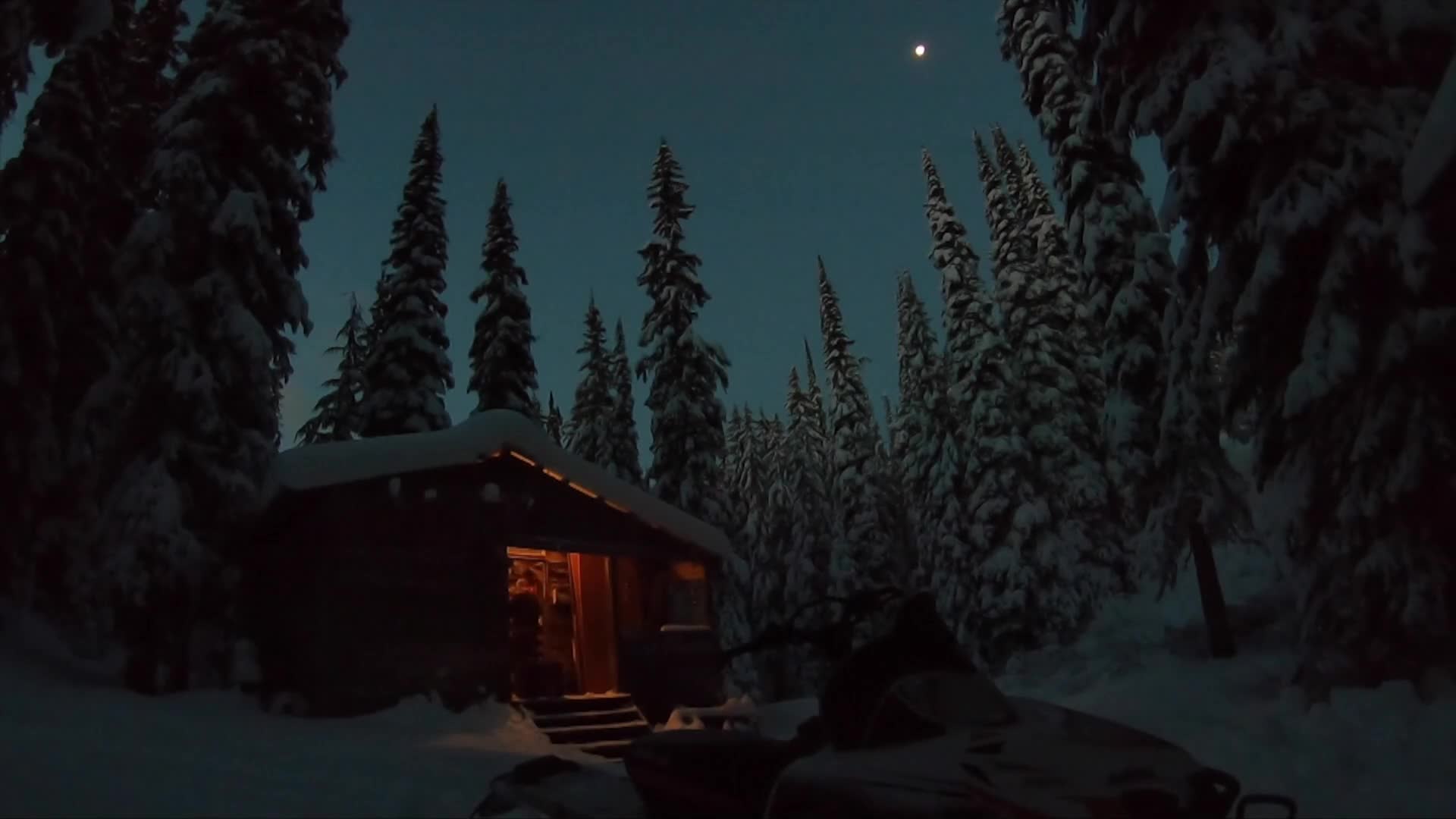A snowmobile sits parked outside a cozy, lit cabin nestled amongst snow-laden fir trees under a twilight sky. The moon hangs high, a pale disc in the deepening blue.