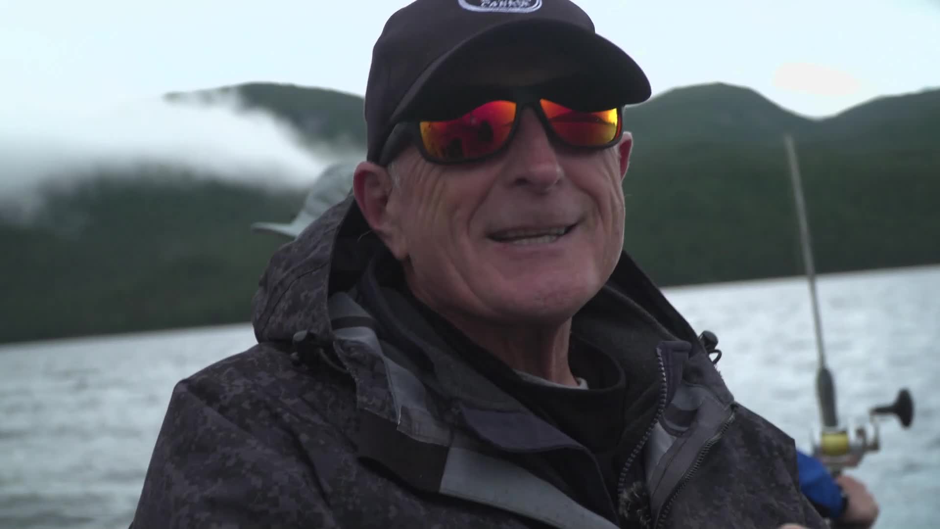 The man in the foreground grins, his sunglasses reflecting the overcast sky. Behind him, a fishing rod bobs on the water, a classic Canadian scene unfolding. The man in the foreground grins, his sunglasses reflecting the overcast sky. Behind him, a fishing rod bobs on the water, a classic Canadian scene unfolding.