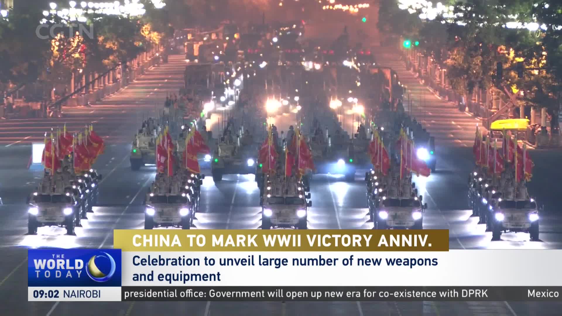 A procession of military vehicles, each adorned with red flags, rolls down a brightly lit street. The CGTN broadcast indicates this is part of a celebration in China.
