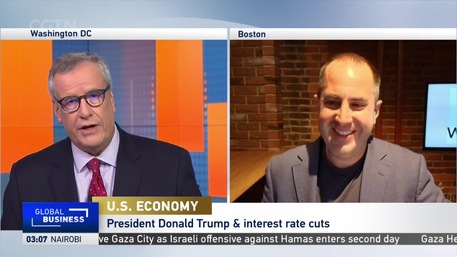A man in a suit and glasses, broadcasting from Washington D.C. on CGTN, is talking. On the right, a man in Boston smiles, appearing on a split screen.
