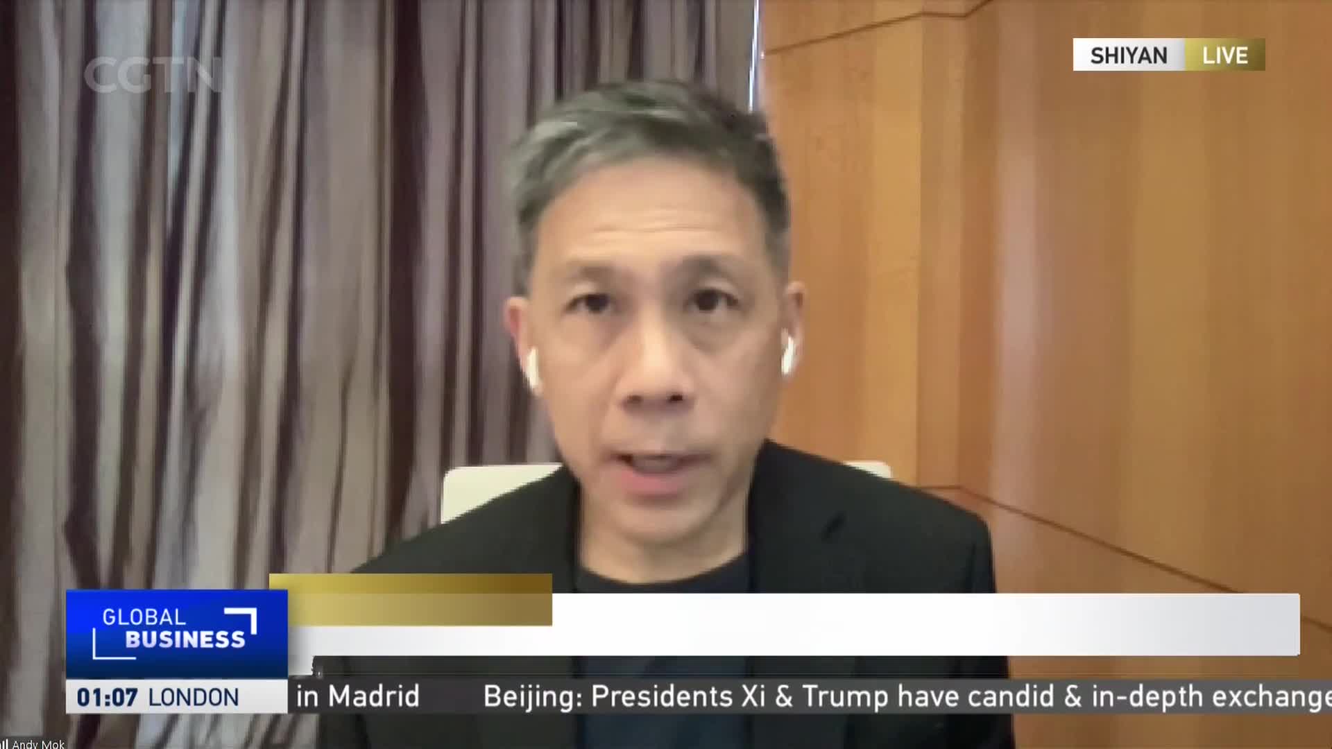 A man with graying hair, wearing earbuds, is speaking directly to the camera. The CGTN logo is visible, and a ticker below reports on a meeting between presidents Xi and Trump.
