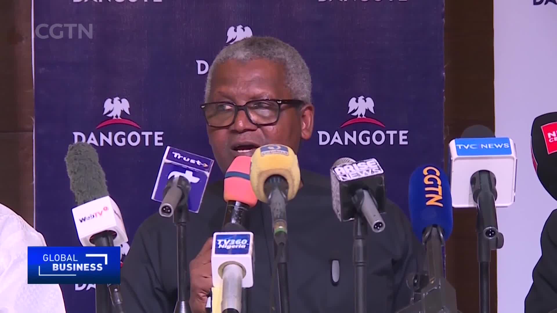 A man in glasses speaks into a forest of microphones, the "CGTN" logo visible on one of them. Behind him is a backdrop with the "Dangote" logo and a crest.
