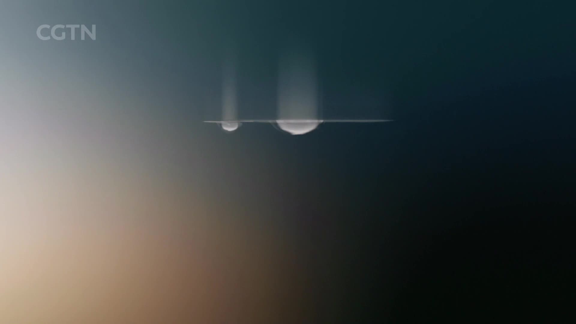 Two large, luminous spheres are emerging from a flat, dark plane.  They are ascending into a gradient of blues and grays, a scene that feels otherworldly, like something you'd see on CGTN.