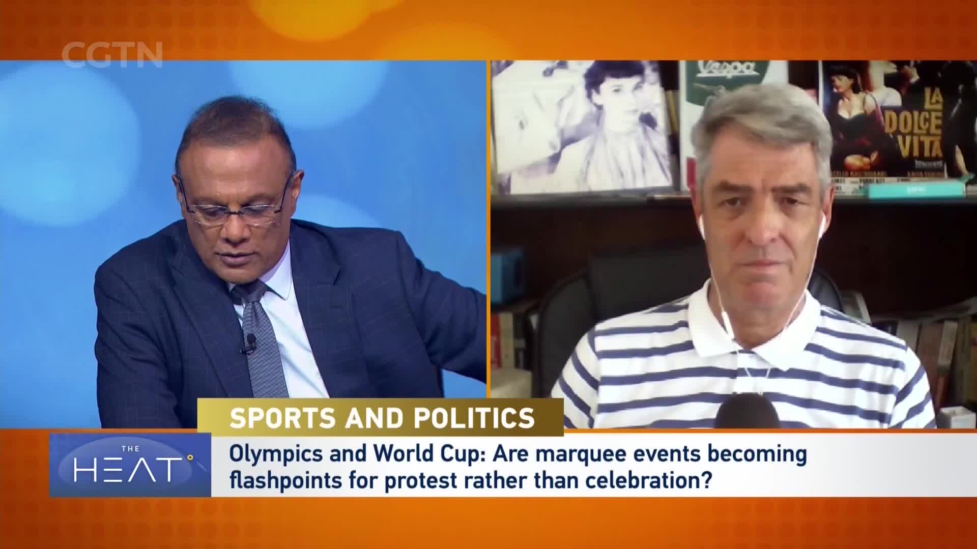 A man in a dark suit and tie looks down at some papers, while another man in a striped shirt speaks directly to the camera. The CGTN logo is visible in the upper left corner of the screen. A man in a dark suit and tie looks down at some papers, while another man in a striped shirt speaks directly to the camera. The CGTN logo is visible in the upper left corner of the screen.