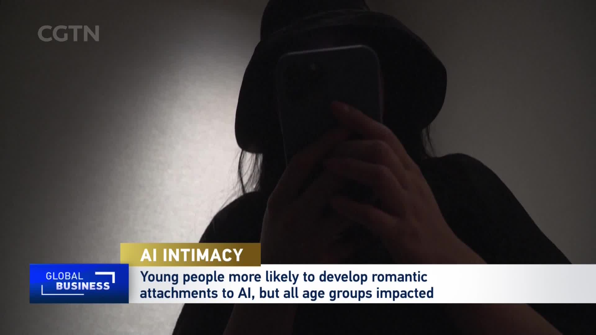 A person, silhouetted and wearing a hat, holds a smartphone up, its screen reflecting light. CGTN's "Global Business" segment is overlaid, discussing AI intimacy. A person, silhouetted and wearing a hat, holds a smartphone up, its screen reflecting light. CGTN's "Global Business" segment is overlaid, discussing AI intimacy.