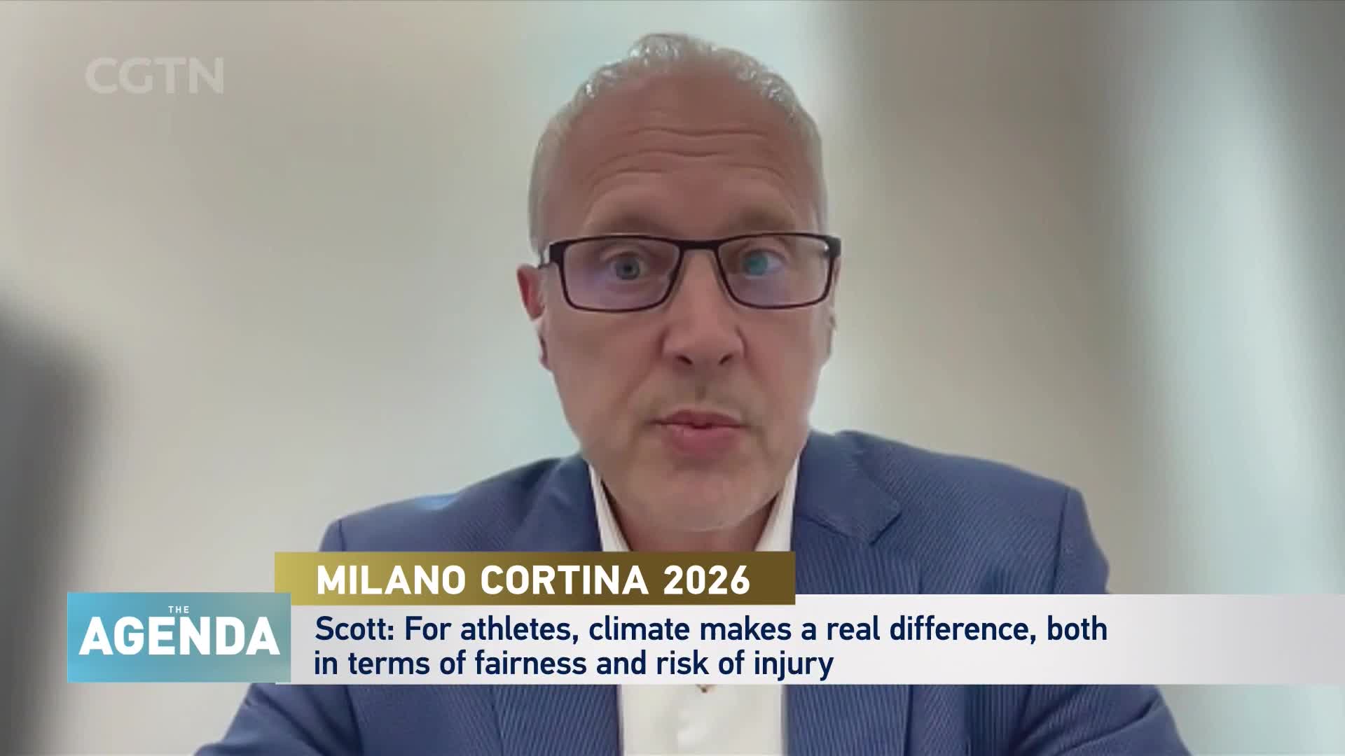 A man in a blue suit and glasses speaks directly to the camera, his words appearing on screen as part of a CGTN broadcast. The text below him discusses how climate impacts athletes, a topic relevant to upcoming events like Milano Cortina 2026. A man in a blue suit and glasses speaks directly to the camera, his words appearing on screen as part of a CGTN broadcast. The text below him discusses how climate impacts athletes, a topic relevant to upcoming events like Milano Cortina 2026.