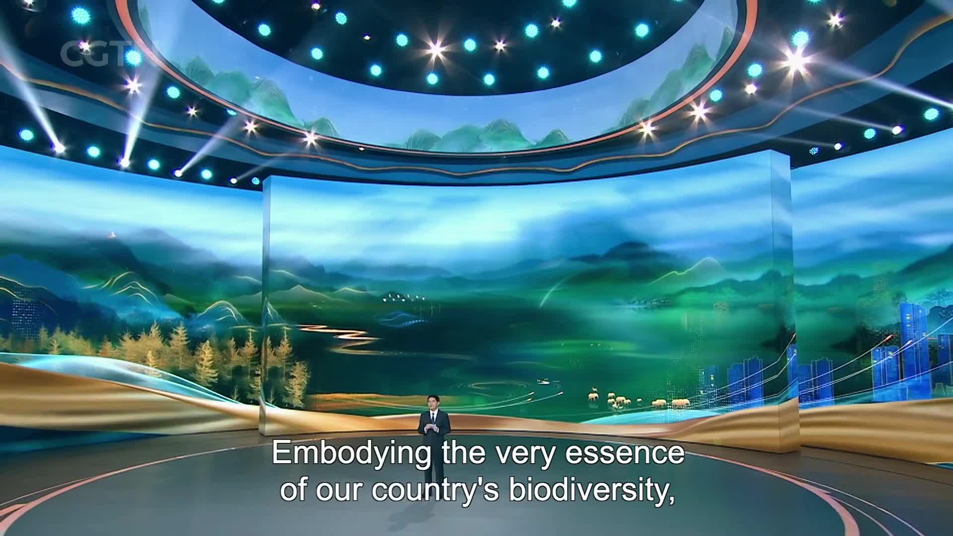 A man stands on a stage, a vast digital landscape of misty mountains and winding rivers unfolding behind him. The CGTN logo is visible on the curved ceiling, hinting at a broadcast from China.