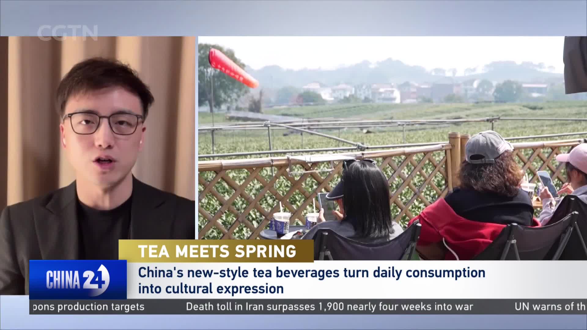 A bright red windsock flutters above a sprawling tea plantation. People relax on chairs, looking out at the fields.