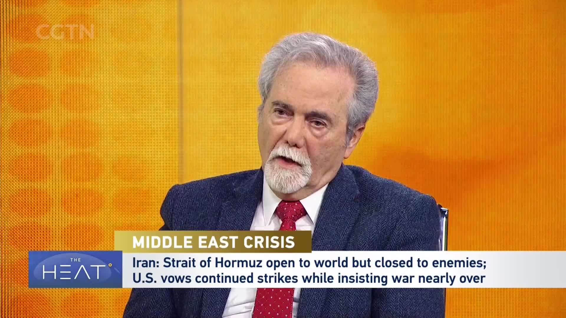 A man with gray hair and a beard speaks into a microphone, his red tie a sharp contrast to his dark jacket. A CGTN graphic displays "MIDDLE EAST CRISIS" and news about Iran and U.S. vows. A man with gray hair and a beard speaks into a microphone, his red tie a sharp contrast to his dark jacket. A CGTN graphic displays "MIDDLE EAST CRISIS" and news about Iran and U.S. vows.