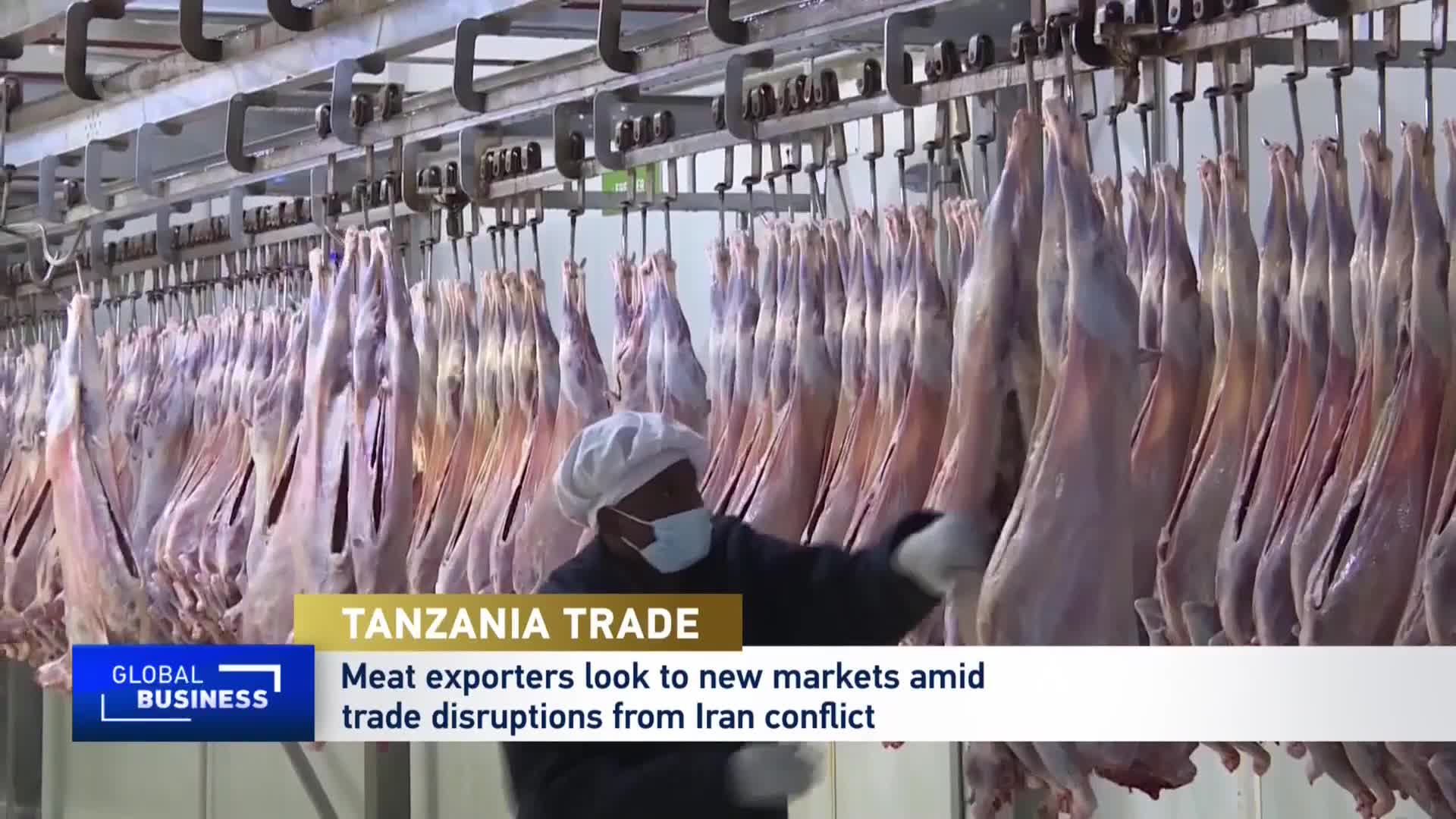 A worker in a white cap and mask inspects rows of carcasses hanging from a metal track. These meat exports from Tanzania are being prepared for new markets. A worker in a white cap and mask inspects rows of carcasses hanging from a metal track. These meat exports from Tanzania are being prepared for new markets.