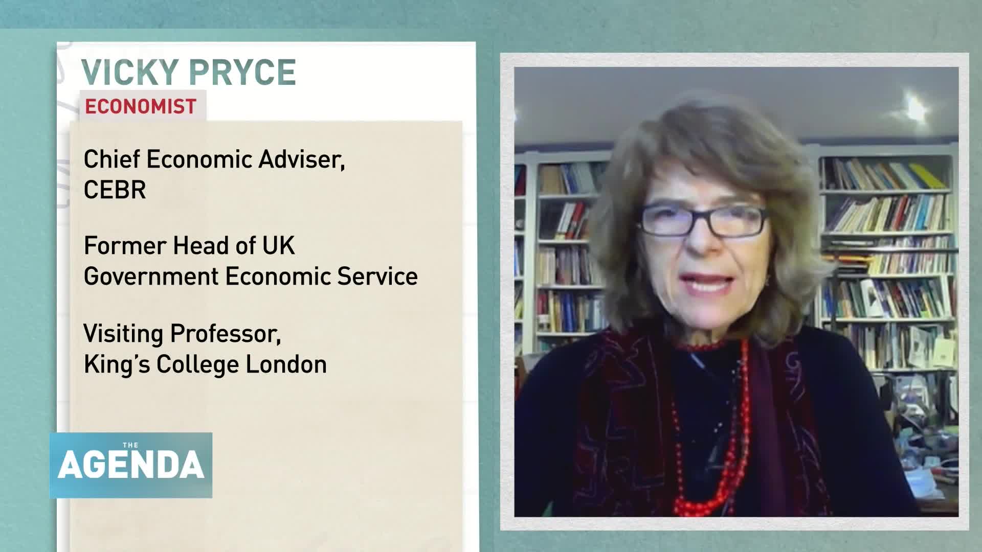 A woman with glasses and reddish-brown hair speaks directly to the camera. Behind her, bookshelves are packed with titles. To the left, text details her credentials as an economist.