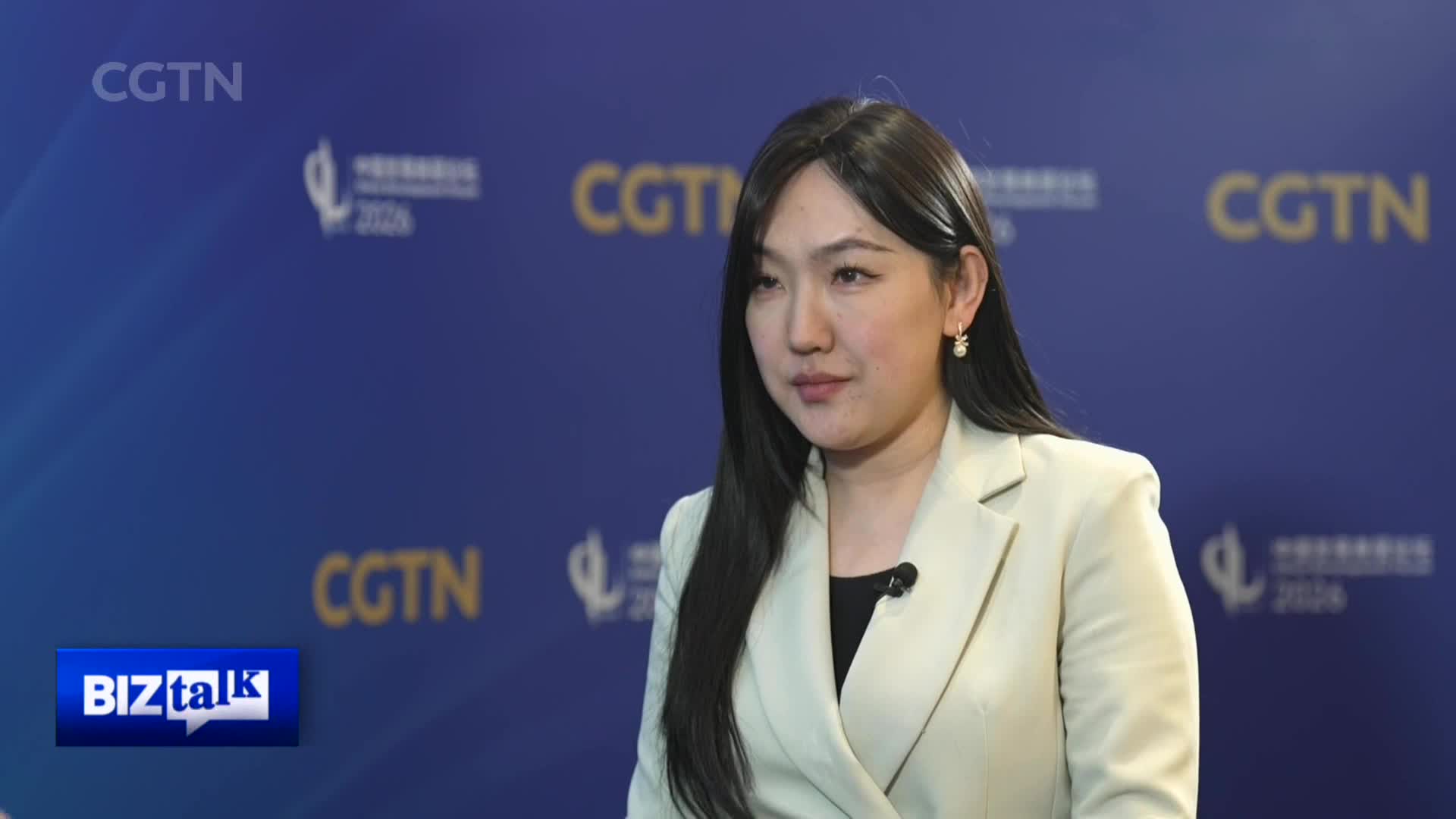 A woman in a light blazer faces forward, her gaze slightly to the side. The CGTN logo appears repeatedly on the blue backdrop behind her. A woman in a light blazer faces forward, her gaze slightly to the side. The CGTN logo appears repeatedly on the blue backdrop behind her.