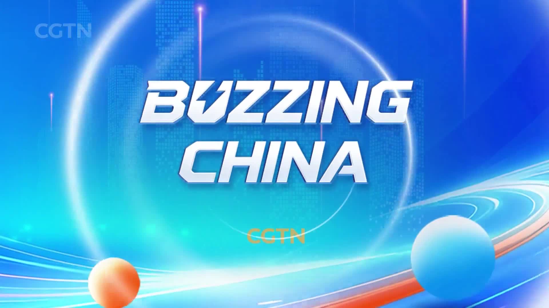 The words "BUZZING CHINA" appear in large, white, metallic letters against a bright blue, digital background. Below them, the CGTN logo is faintly visible, and two glowing spheres, one orange and one blue, float in the foreground.