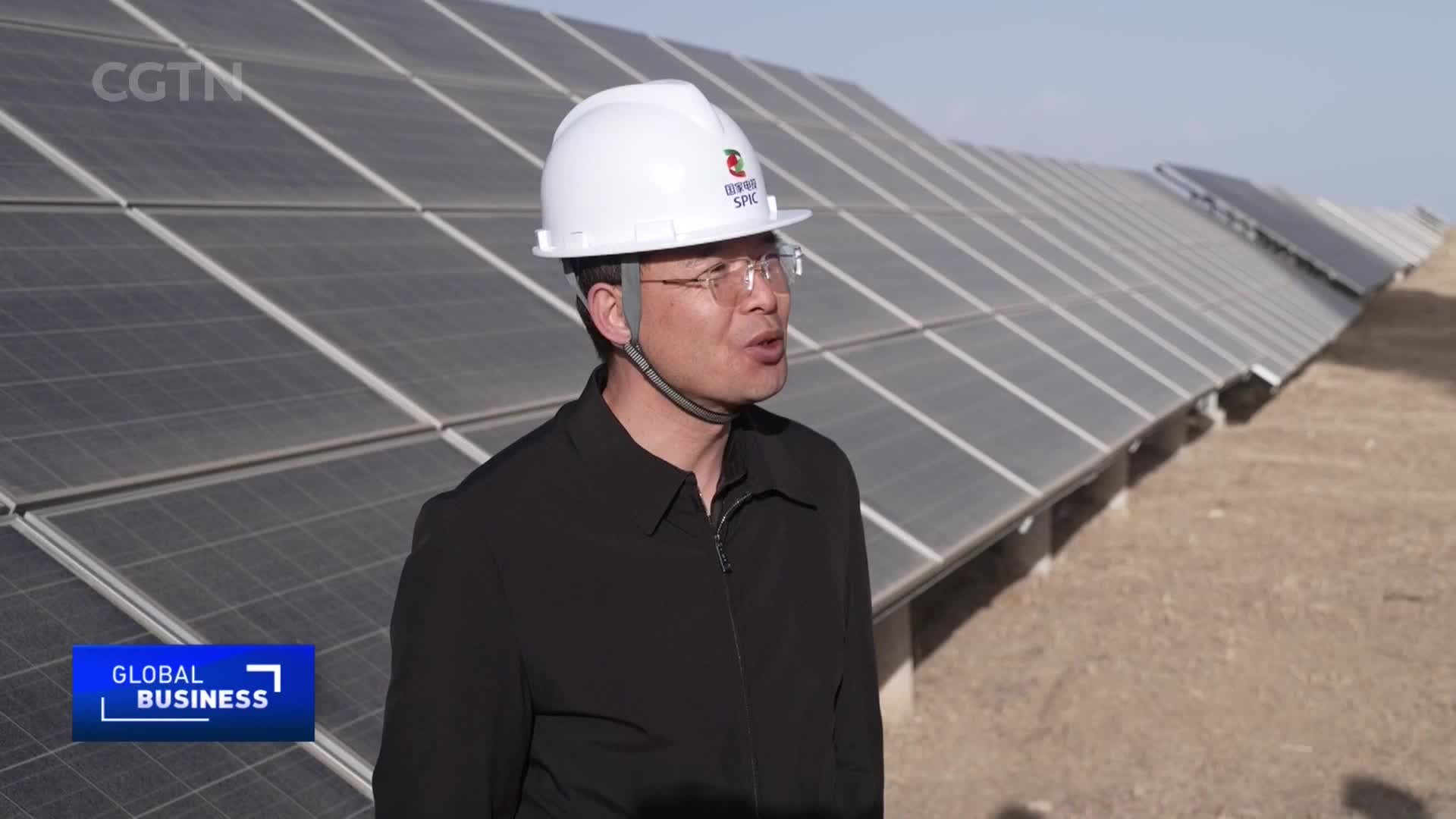 A man in a white hard hat speaks in front of rows of solar panels stretching into the distance. The CGTN logo appears in the upper right corner.