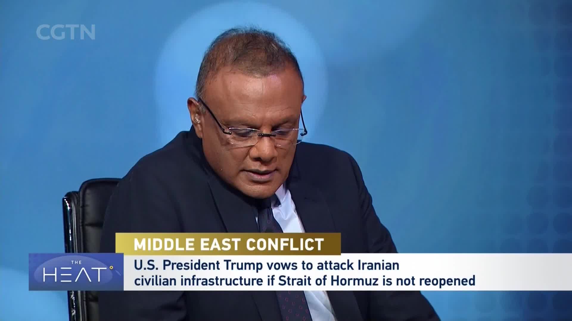 A man in a suit and glasses looks down at a screen, his face illuminated by the blue background of the CGTN studio. Text below him reads "MIDDLE EAST CONFLICT" and "U.S. President Trump vows to attack Iranian civilian infrastructure if Strait of Hormuz is not reopened."