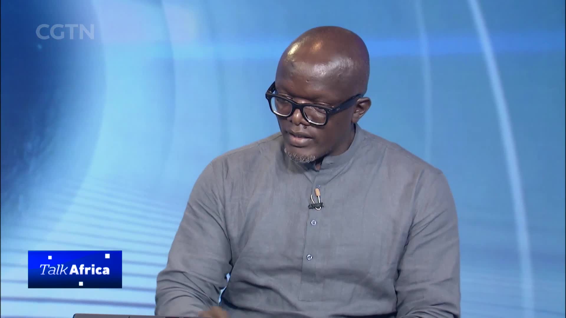 A man with glasses and a grey shirt sits in front of a blue background with the CGTN logo. A graphic for "Talk Africa" appears in the lower left corner.