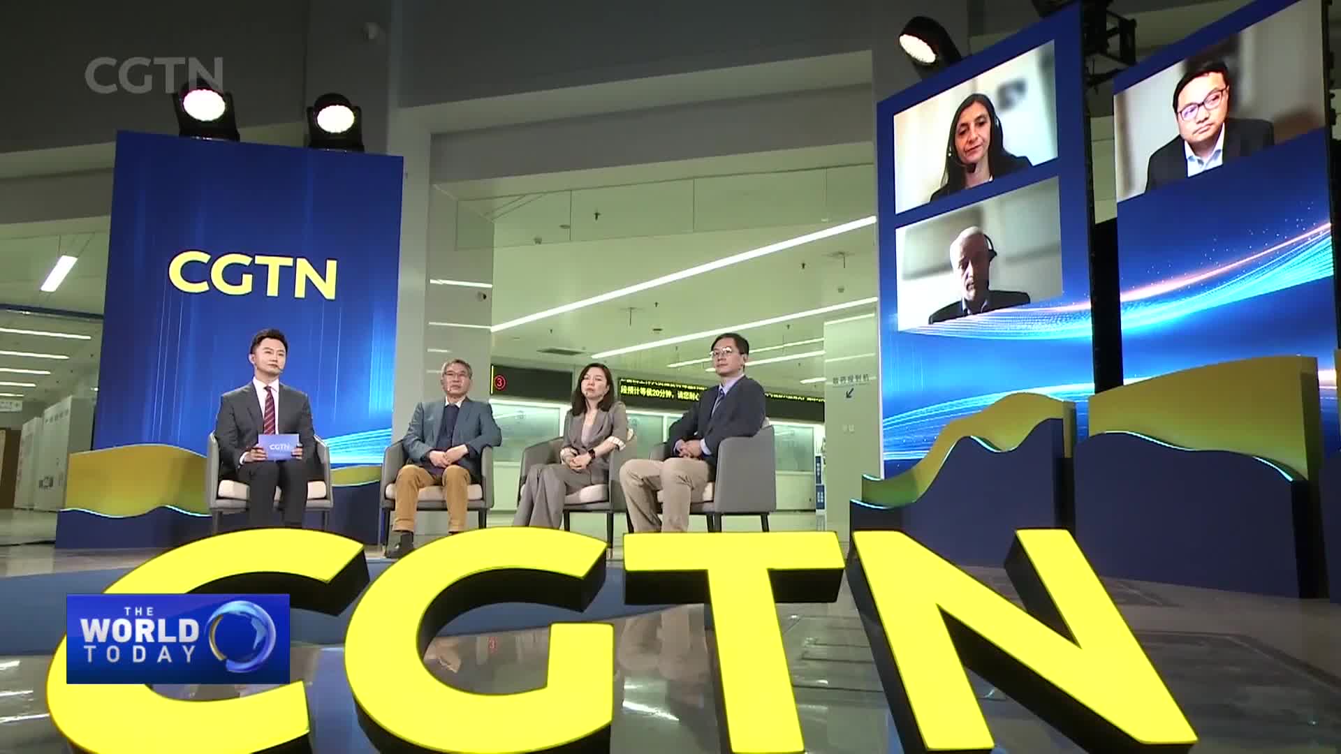 A panel of four people are seated on a stage, with three present in the studio and one appearing on a screen. The CGTN logo is prominently displayed behind them.