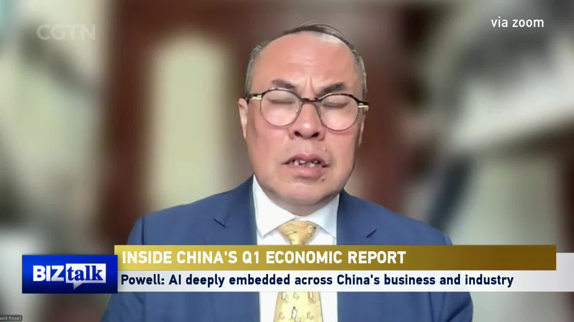 A man in a blue suit and yellow tie speaks with his eyes closed, his glasses perched on his nose. A CGTN "Biztalk" graphic overlays the bottom of the screen, indicating a discussion about China's Q1 economic report and AI's integration into its industries.