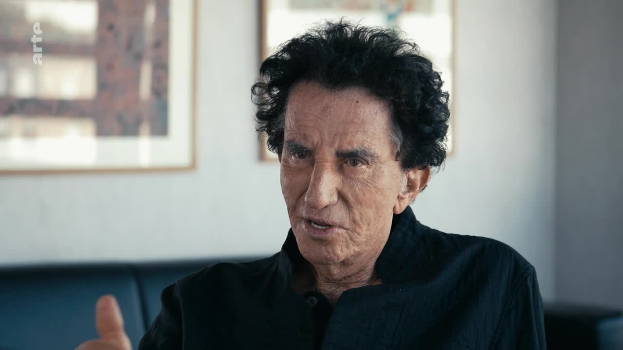 A man with dark, curly hair gestures with his right hand while speaking. The arte logo is visible in the upper left corner, suggesting a French television program.
