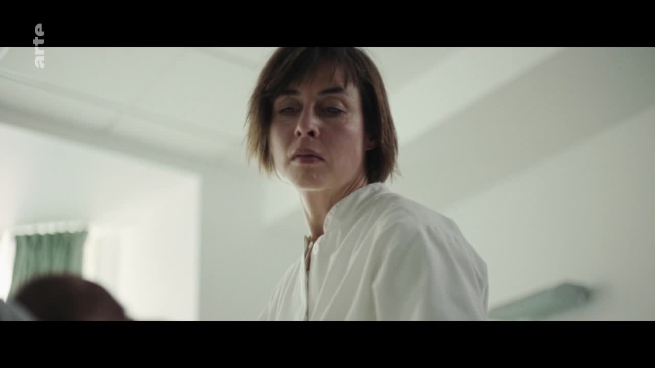 A woman in a white shirt looks down, her expression a mix of exhaustion and concern. The arte logo subtly marks the scene, suggesting a French production.
