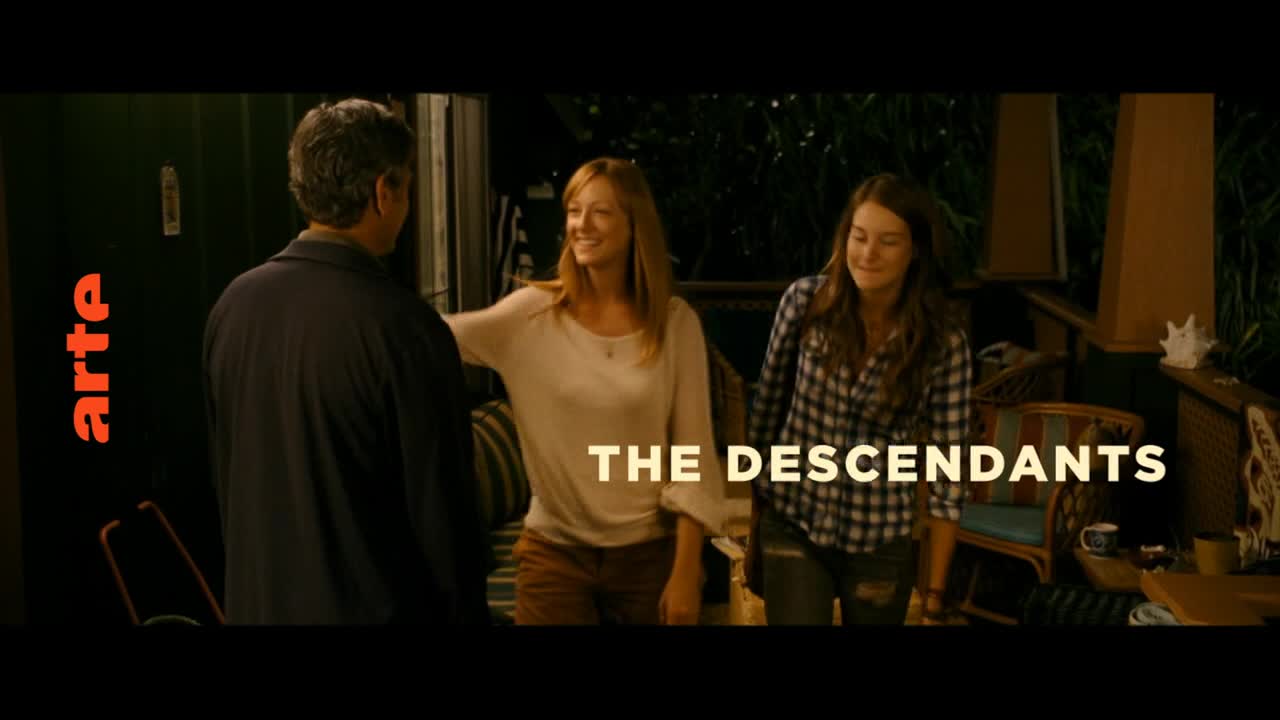 A man in a dark jacket turns to face two women on a porch. The woman in the middle smiles, her hand reaching out. The woman on the right, wearing a plaid shirt, looks down.