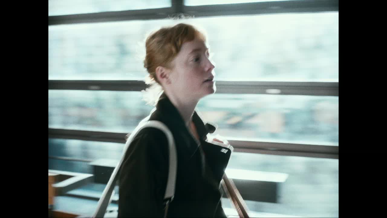 A woman with auburn hair walks past a window, her gaze fixed ahead. The light catches her profile as the French landscape streaks by outside.