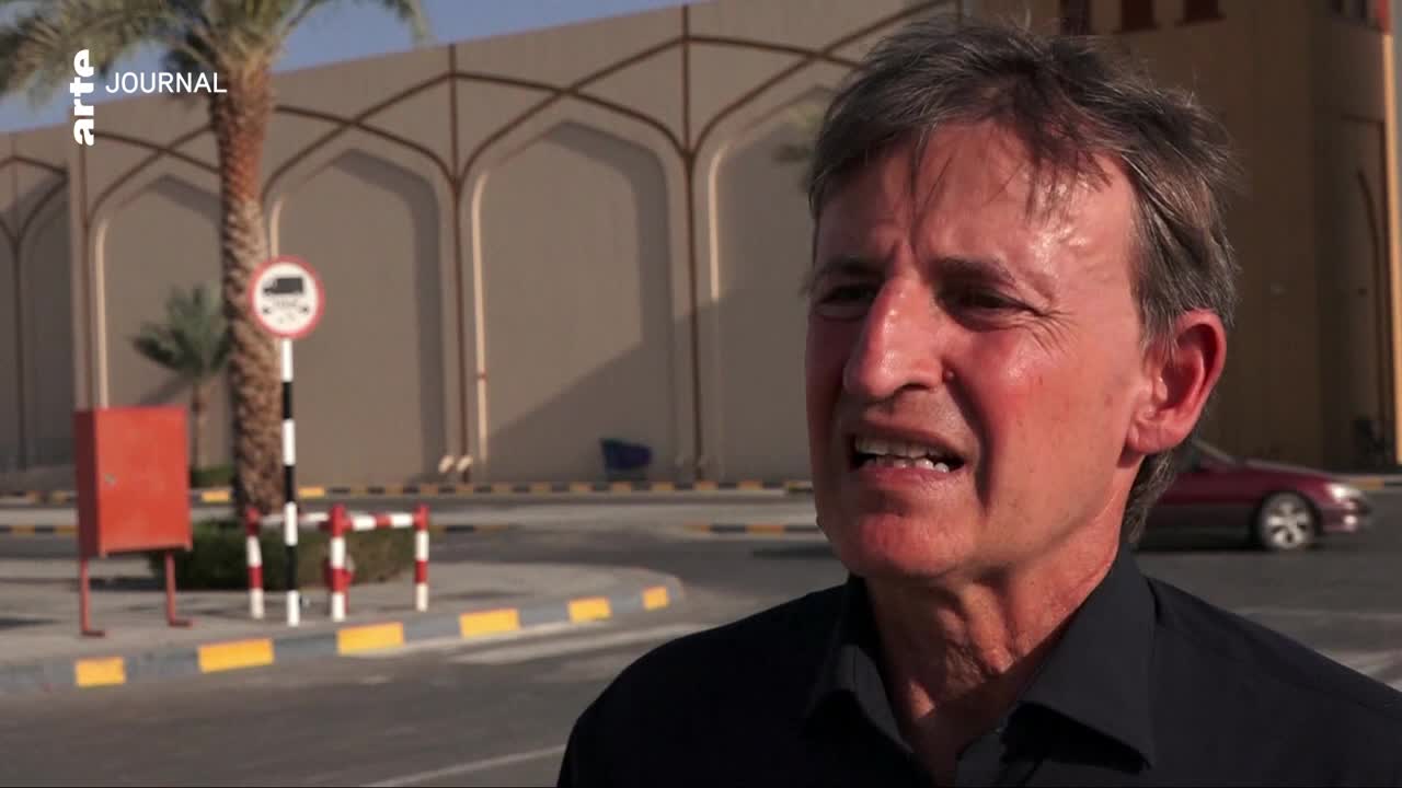 A red sedan drives past on the street, its wheels a blur against the pavement. The man in the foreground speaks, his face etched with emotion, while the arte JOURNAL logo is visible in the upper left corner.