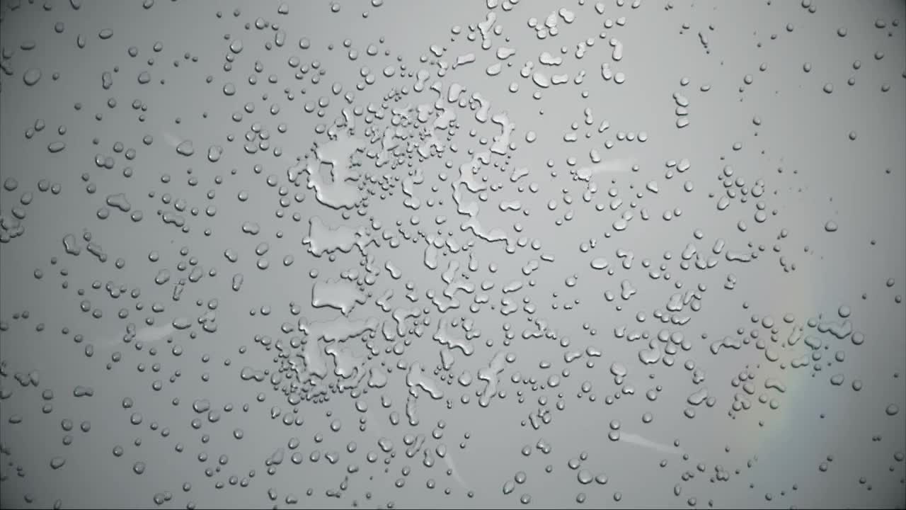 Raindrops cling to the glass, distorting the view of a pale sky. A faint arc of color, a hint of rainbow, appears in the distance.