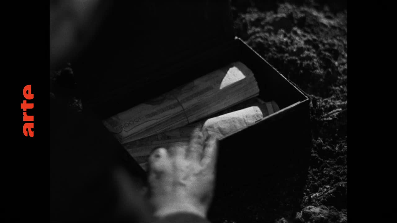 A hand reaches into a dark box filled with rolled-up papers. The papers, bound with string, are stacked unevenly, hinting at their value.