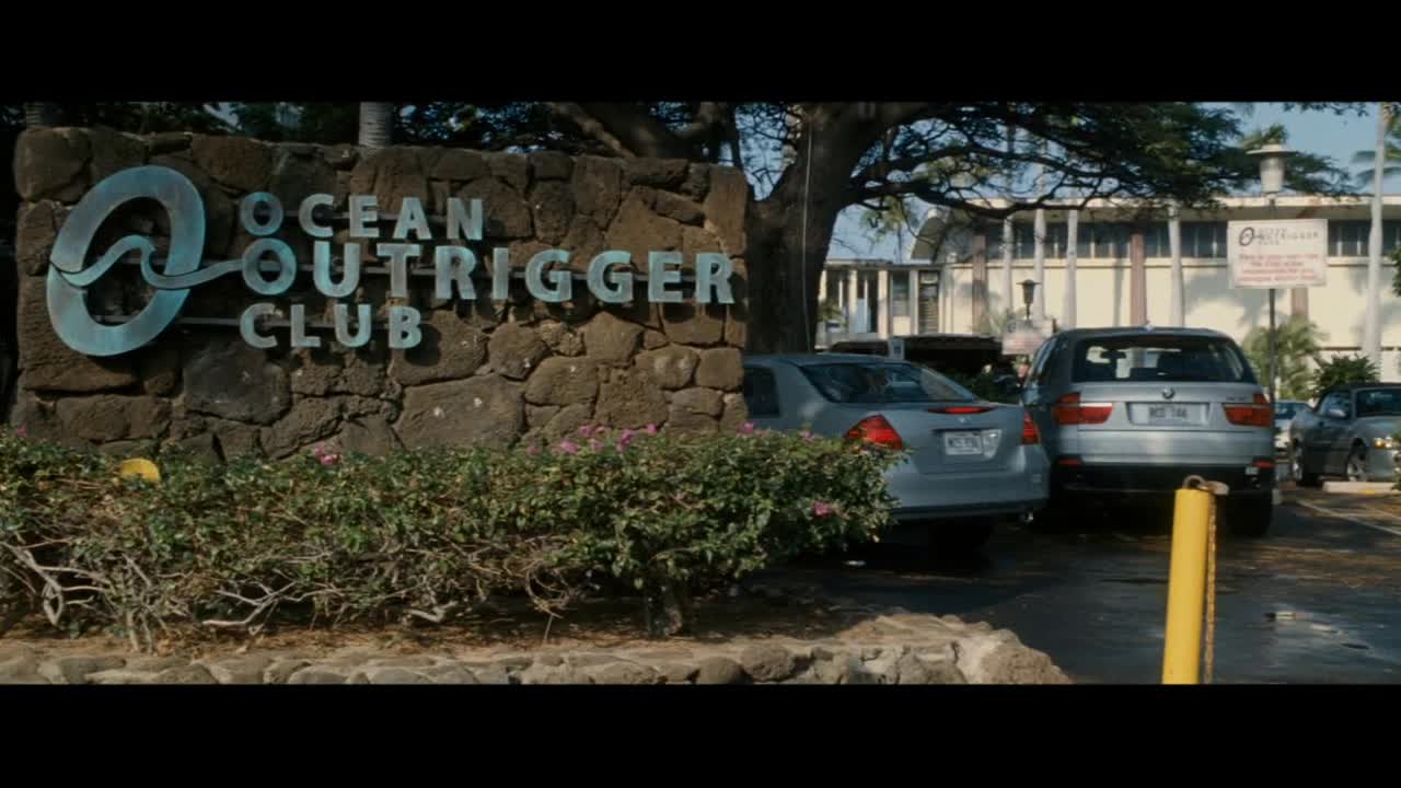 A silver sedan pulls up to the Ocean Outrigger Club entrance. A silver SUV is parked just behind it.