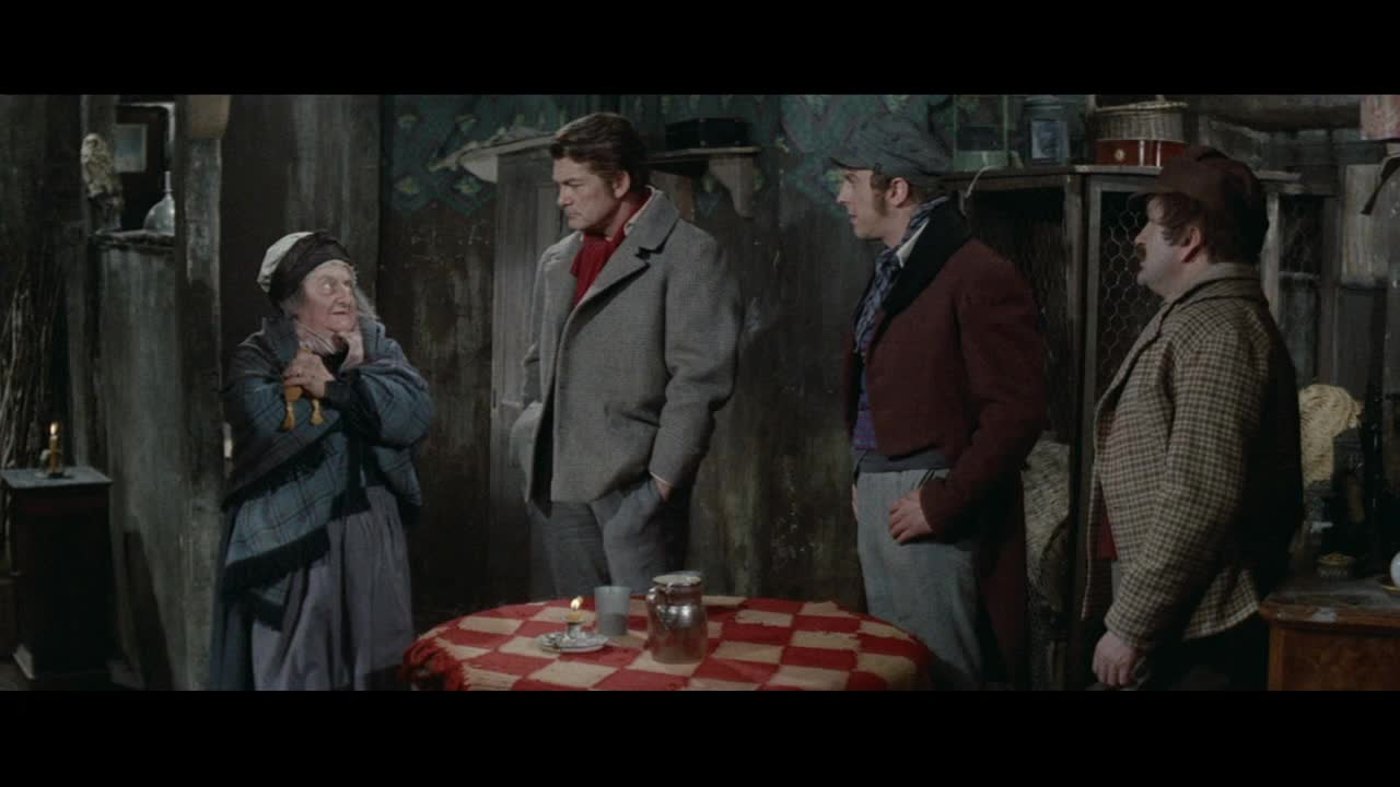 An elderly woman, her face etched with a lifetime of stories, clutches two wooden figures. Three men stand before her, their expressions a mix of curiosity and concern, as if they've stumbled into a scene from a classic French film.