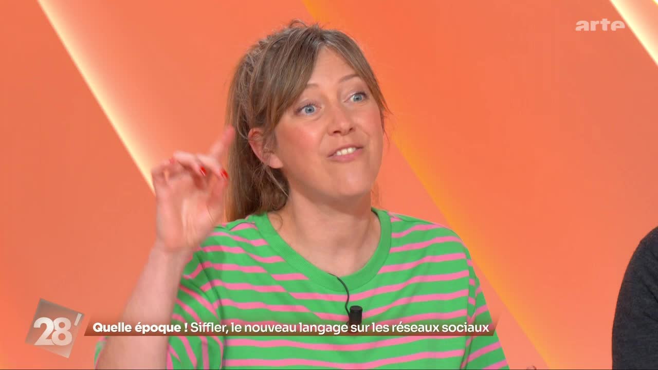 A woman with blonde hair pulled back in a ponytail gestures with her right hand, her index finger pointing upwards. She wears a bright green t-shirt with thin pink stripes. The background is a warm, peachy orange with a diagonal light beam.